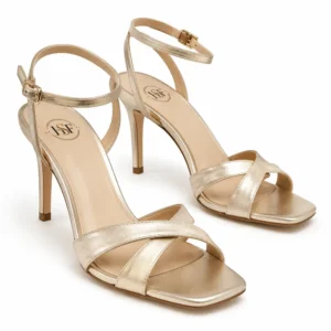Private label metallic cross strap ankle stiletto sandal in soft champagne metallic finish, shown in a front three-quarter hero view for wholesale, private-label and B2B footwear sourcing.